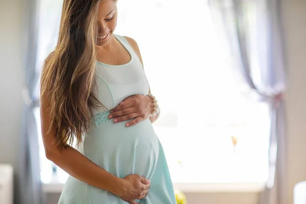 Femme enceinte souriante en robe avec ses mains au ventre — Photo