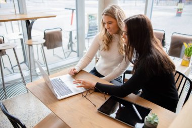 Arkadaşlar kafede dizüstü bilgisayarda okul projesini tartışıyor.