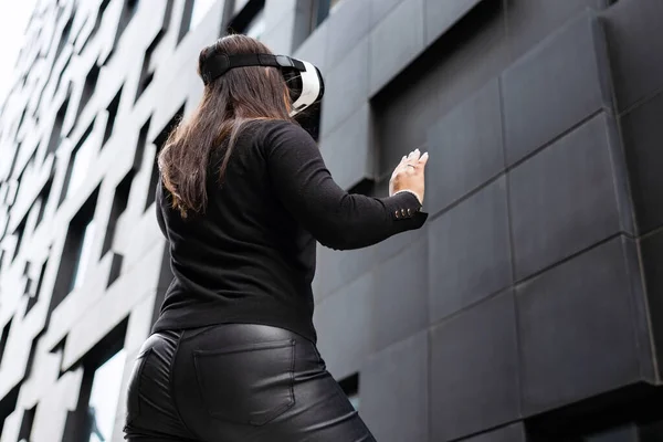 Voltar de mulher vestindo óculos de tecnologia de realidade virtual contra a construção moderna — Fotografia de Stock
