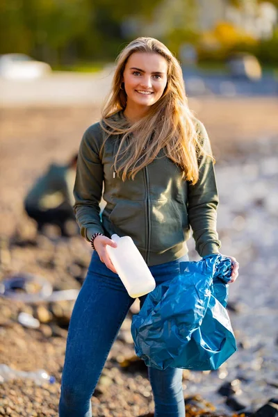 Улыбающаяся женщина-волонтер держит бутылку и мешок для мусора на пляже — стоковое фото
