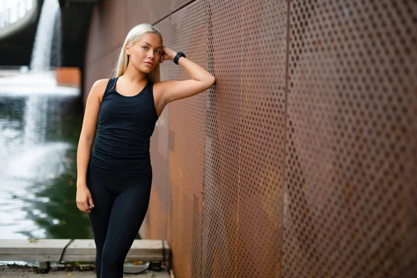 Mujer hermosa ajuste en ropa deportiva apoyándose en la pared metálica después del entrenamiento —  Fotos de Stock