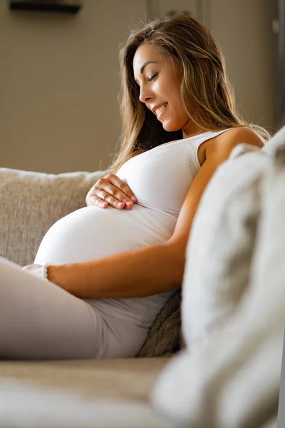 Femme enceinte souriante assise dans un canapé regardant son estomac — Photo