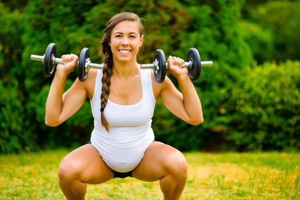 Mujer embarazada sonriente haciendo sentadilla al hombro prensa usando sombrillas —  Fotos de Stock