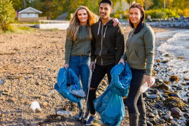 Gülümseyen gönüllüler, plajda çöp torbası tutan arkadaşlar.