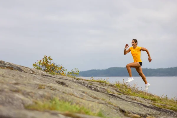 Side view of fitness woman doing high-intensity running on mountainside by the sea — Stock Photo, Image