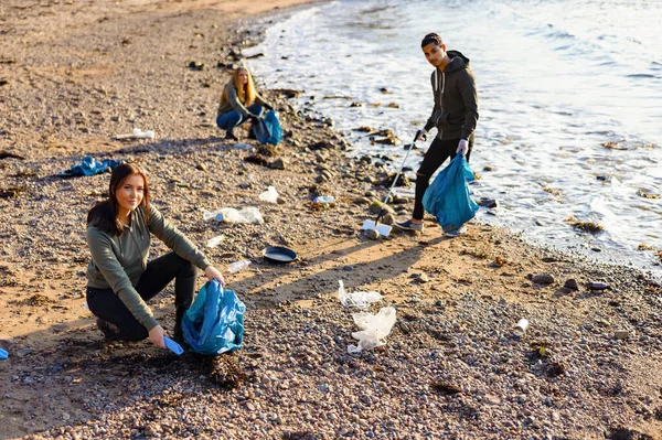 Mujer joven en un equipo recogiendo basura plástica en bolsa en la playa — Foto de Stock