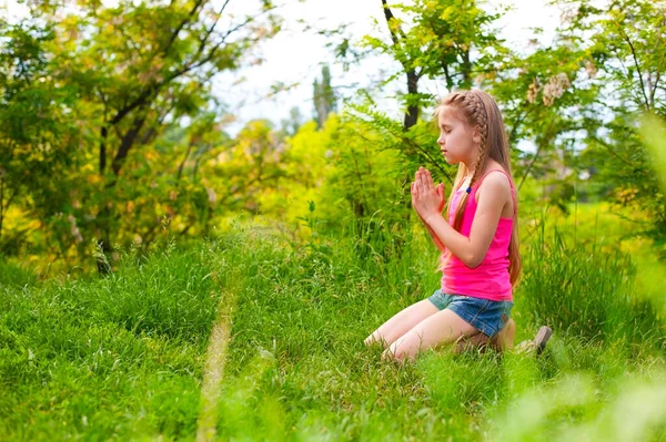 The girl prays to God in the nature. She is kneeling on green grass