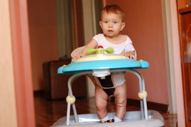 Küçük bir çocuk bebek yürüyenlerin içinde oturur ve gülümser.