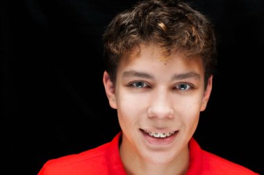 Siyah arka planda diş teli takan bir çocuğun dramatik portresi. Dişlerindeki diş telleri açıkça görülüyor.