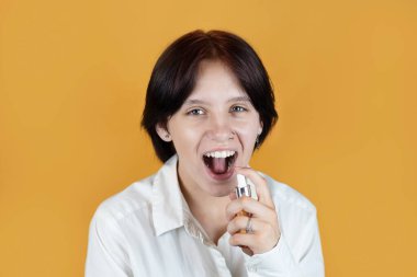 Modern bir genç kız turuncu arka planda gülümsüyor ve elinde bir şişe ferahlatıcı gargara, ağız tazeleyici tutuyor. Ağız gargarası temizleyicisini ağız sağlığı ve hoş koku için kullanıyor.