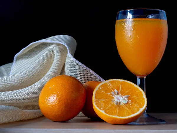 Half oranges are placed on a sack on the table, with glass of or