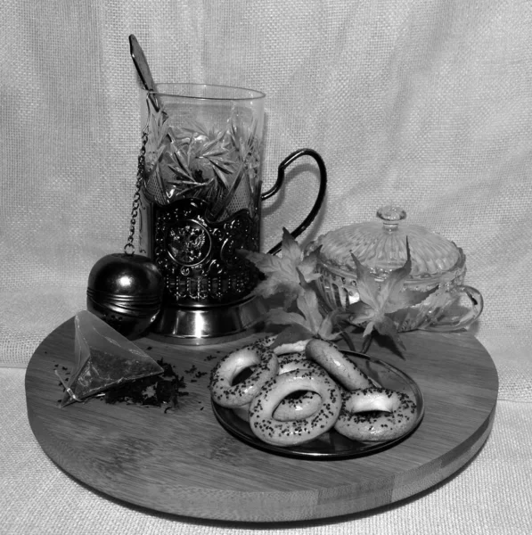 Russian tea, a glass in a silver cup holder, black tea, bagels with poppy seeds on a wooden tray. black and white photography.