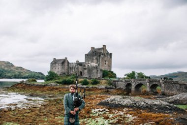 Dornie, İskoçya; 27 Ağustos 2019: Eilean Donan Kalesi'nin üzerinde müzik aletini çalan İskoç gaydacısı