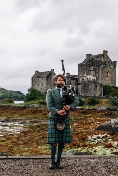 Дорни, Шотландия; 27 августа 2019 года: шотландский волынщик играет на своем музыкальном инструменте над замком Эйлиан Донан — стоковое фото