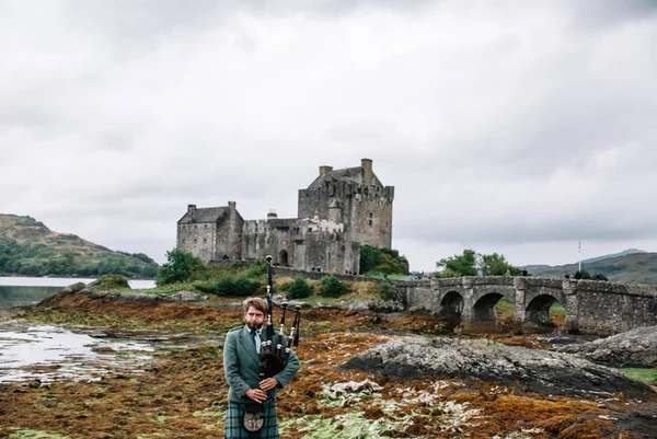 Дорни, Шотландия; 27 августа 2019 года: шотландский волынщик играет на своем музыкальном инструменте над замком Эйлиан Донан — стоковое фото