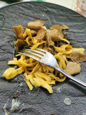 A sophisticated dish featuring fresh black tagliolini pasta delicately infused with the earthy aroma of shaved black truffle, served on a sleek black plate for an elegant presentation.