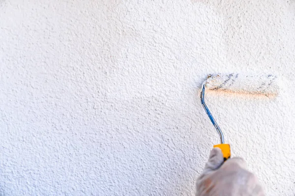 Man painting the wall of the house. Hand holding a roller with white paint. Concept of painting and reforming the house.