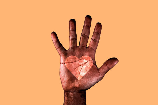 Open palm of a African American man with a heart drawn asking for the stop of racism. Black hand isolated on a orange background.