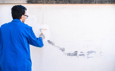 Boyacı boya silindiriyle beyaz bir duvar boyamaya çalışıyor. Evin köşelerini boyama ve ıslah etme kavramı.