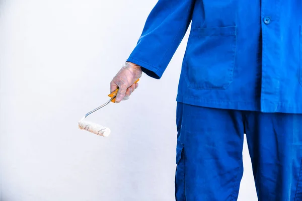 Hand of anonymous painter in a blue uniform holding a paint roller. Closeup view of painter.