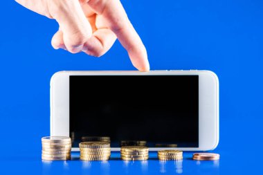 Mavi arka planda bozuk para yığını olan bir cep telefonu. İş büyümesi ve finansal tasarruf kavramı. Kopyalama alanı için siyah ekranlı cep telefonu.