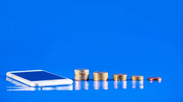 Mobile phone with stack of coins on blue background. Business growth and financial saving concept of money.
