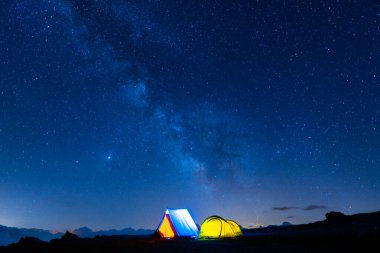 Gece Samanyolu 'nun altında parlayan iki kamp çadırı. Yıldızlı sihirli gökyüzünün altında, dağlarda kamp yapmak. 5 Milyar Yıldız Oteli.