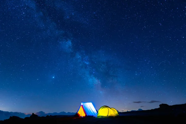 Two camping tents glowing under the milky way at night. Camping in the mountains under the starry magical sky. 5 Billion Star Hotel.