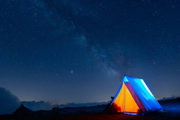 Ridge tent glowing under the milky way at night. Camping in the mountains under the starry magical sky. 5 Billion Star Hotel.
