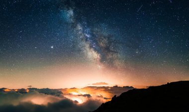 Şehir ve köylerin ışıkları altında turuncu ışık kirliliği yaratan bulutlardan oluşan bir denizin üzerindeki yıldızlı gökyüzü. Samanyolu ile uzun süreli manzaraların gece fotoğrafları..