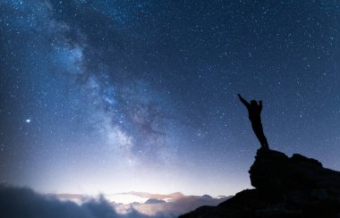 Kolları havada olan ve evrenin sonsuzluğunu düşünen bir insan. Samanyolu ve yıldızlı sihirli gökyüzünün altında bir adamın silueti. Gerçek bir açık hava macerası ve vahşi yaşam konsepti.