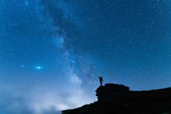 Dağda kollarını kaldırmış genç bir adamın silueti. Mavi gece yıldızlı gökyüzü ile arka planda seyahat et..