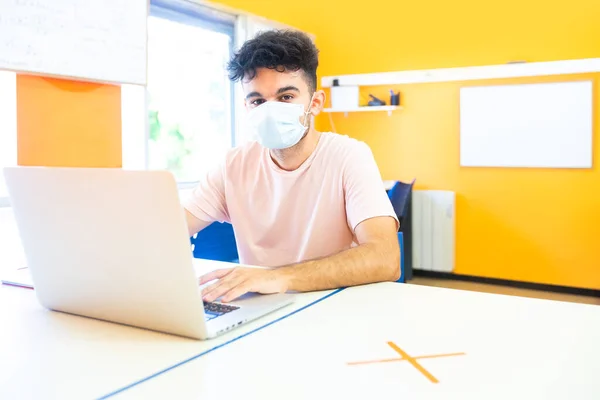 Young student with medical face mask doing class with his laptop at school. Going back to school after the coronavirus epidemic.