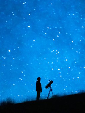 Astronom evrenin ve yıldızların büyüklüğünü gözlemliyor. Geceleri mavi yıldızlı gökyüzünü gözlemleyen teleskoplu bir astronomi aşığının silüeti..