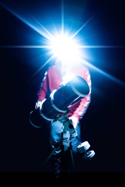 Gecenin karanlığında teleskop ve farlı bir adam yıldızları gözetliyor. Astronomi aşığı teleskopla geceleyin yıldızlı gökyüzünü izliyor..