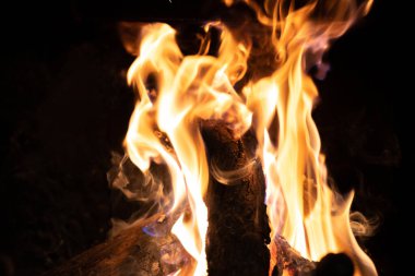 Şöminede parlak ve güçlü turuncu alevlerin içinde yanan odun kütükleri. Yangının detaylı görüntüsü..