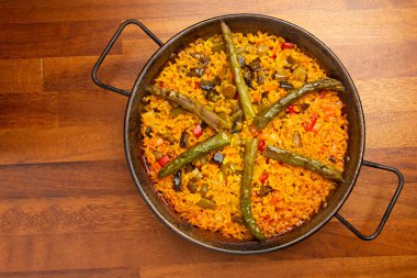 Paella tavasında sebzeli paella pilavı, ahşap arka planda..
