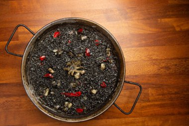 Ahşap arka planda, paella tavasında kalamar olan siyah pirinç.