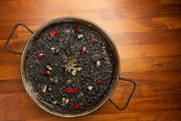 Ahşap arka planda, paella tavasında kalamar olan siyah pirinç.