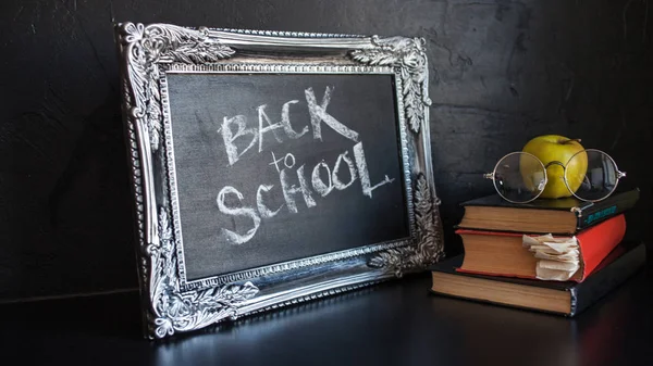 Back to school, text on chalkboard and a stack of textbooks. Textured vintage frame on a dark textured background. — Stock Photo, Image
