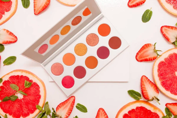 Lindo piso con paleta de cosméticos con fruta fresca, fresas cortadas y pomelo o naranja roja, hojas de menta — Foto de Stock