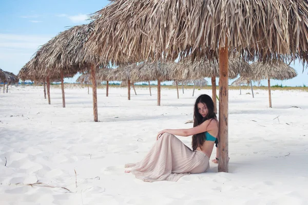 Jeune femme séduisante en vacances à la mer, assise sur le sable sous un parapluie de paille . — Photo