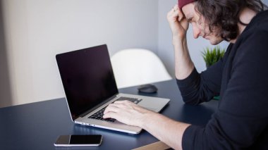 Bir dizüstü bilgisayar için tasarımcı, serbest çalışanlar için bir işyeri. Masada oturan genç bir adam.