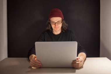 İşyerinde tasarımcı veya programcı. bir şapka ve gözlük bir dizüstü bilgisayarda oturan genç adam.