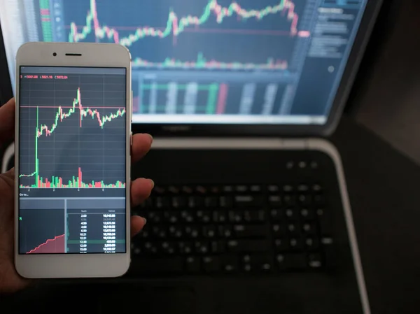 Servizi multipiattaforma per il trading in borsa. Mano con il telefono sullo sfondo di un computer portatile — Foto Stock