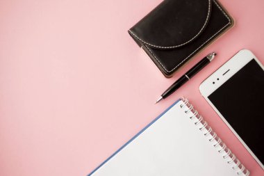 Kırtasiye, beyaz akıllı telefon, kalem, cüzdan, saat, takvim, defter. Pembe arka plan.