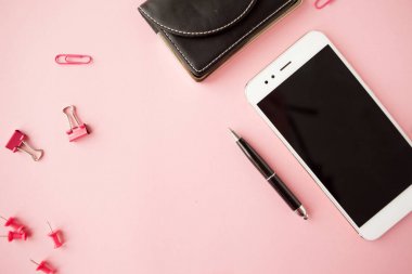 Kırtasiye, beyaz akıllı telefon, kalem, cüzdan, saat, takvim, defter. Pembe arka plan.