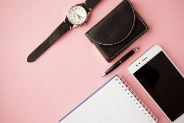 Kırtasiye, beyaz akıllı telefon, kalem, cüzdan, saat, takvim, defter. Pembe arka plan.