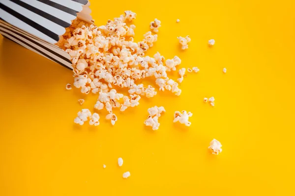 Popcorn in paper bag scattered on yellow background top view — Stock Photo, Image