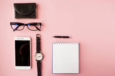 Kırtasiye, beyaz akıllı telefon, Gözlük, kalem, cüzdan, saat, takvim, defter. Pembe arka plan.